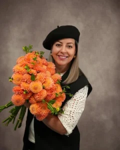 Tooka Florist owner holding a large bouquet of orange dahlias wearing a black beret