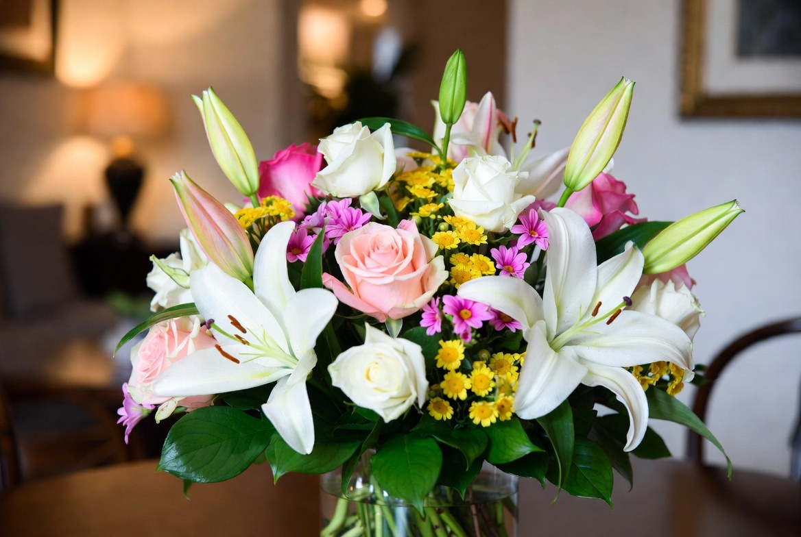 Elegant home flower arrangement with white lilies pink roses and yellow chrysanthemums in a glass vase