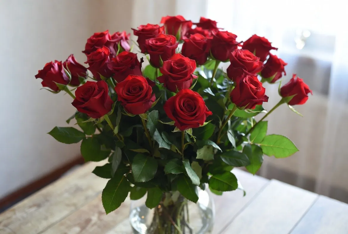 Classic Valentine's Day bouquet of long-stem red roses in a glass vase on a wooden table